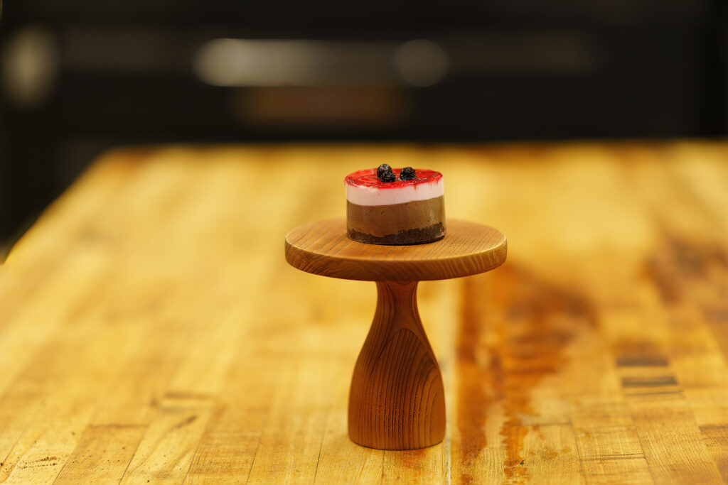 Single layered berry cheesecake on a turned wooden cake stand at Arlington Bakery.