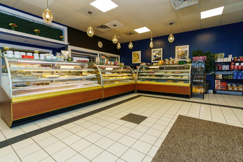 Interior of Arlington Bakery with L-shaped glass pastry cases, pendant lights and navy blue walls.