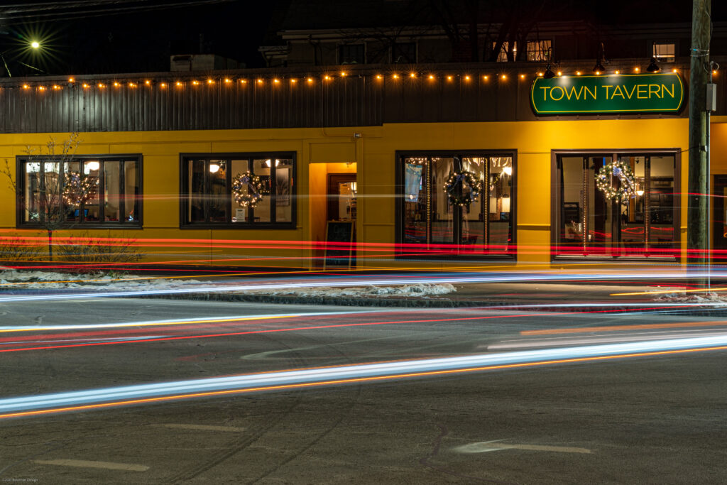 Town Tavern's yellow facade at night with long-exposure light trails from a passing MBTA bus, Arlington MA.