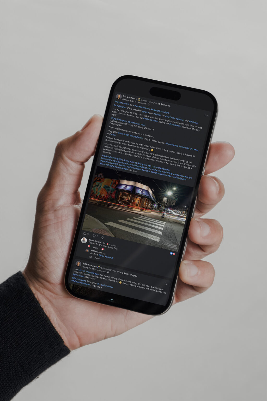 Hand holding a phone showing an Arlington at Night Facebook post with a night storefront photograph.