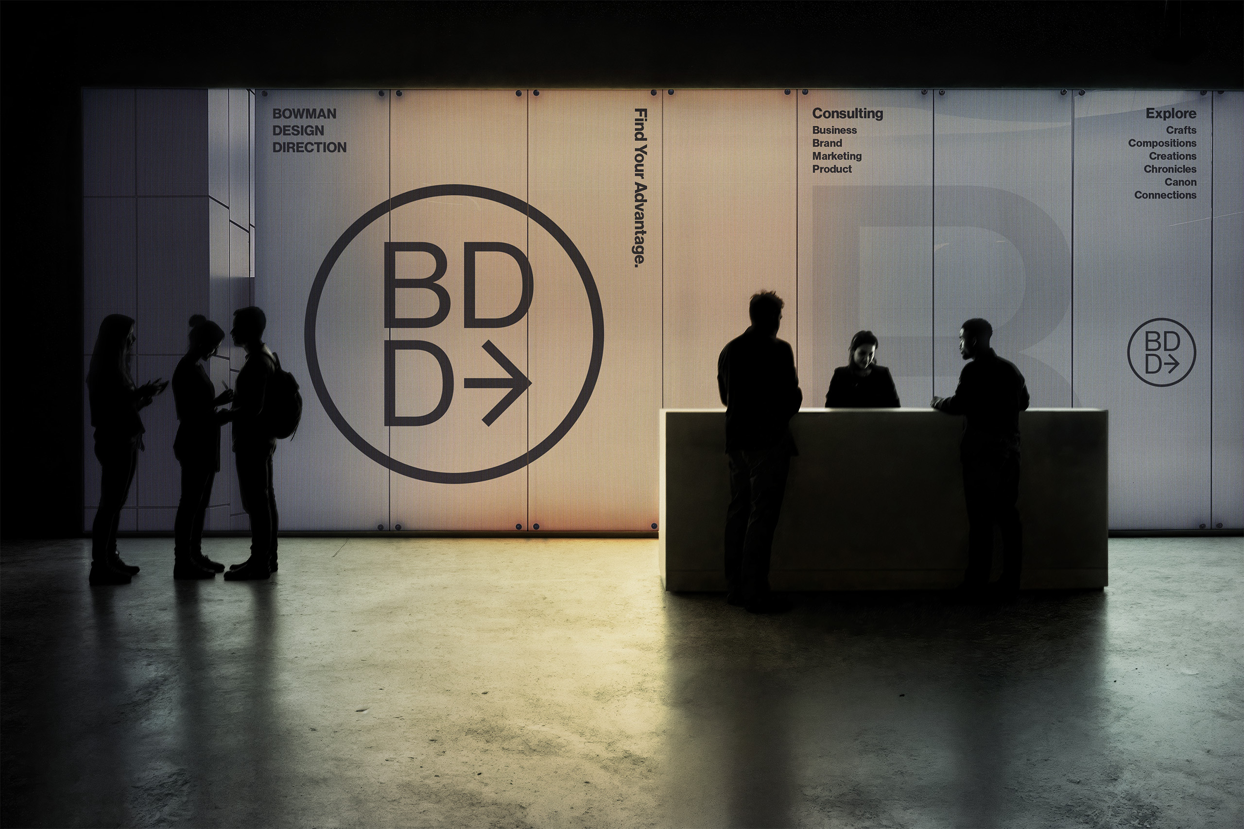 Lobby with the large BDD circle mark printed across a backlit wall beside Find Your Advantage, Consulting, and Explore wayfinding text, silhouetted visitors gathered at a white reception desk.