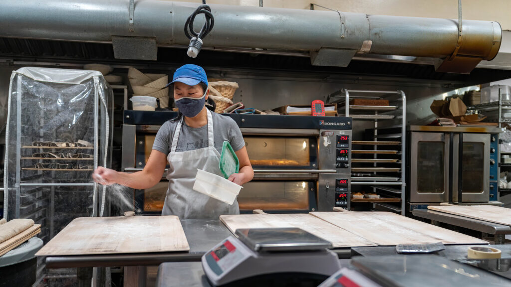 Daisy Chow dusting flour over a wooden work board in the Breadboard Bakery kitchen.