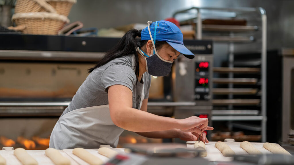 Close view of Daisy Chow shaping baguette dough by hand at Breadboard Bakery.
