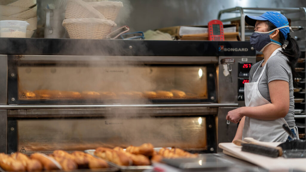 Steam rising from the open deck oven as baguettes bake at Breadboard Bakery.
