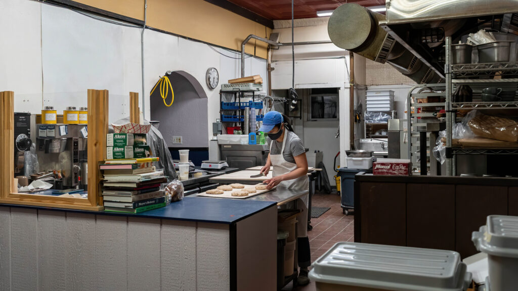 Baker Daisy Chow shaping dough on a steel table in the Breadboard Bakery kitchen.