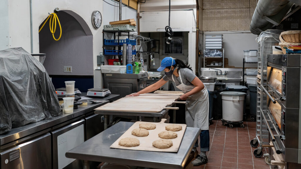 Daisy Chow leaning over a table of shaped sourdough rounds in the Breadboard Bakery kitchen.