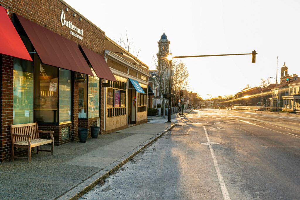 Butternut Bakehouse red awnings on Massachusetts Avenue at sunrise, empty street and church steeple in the distance.