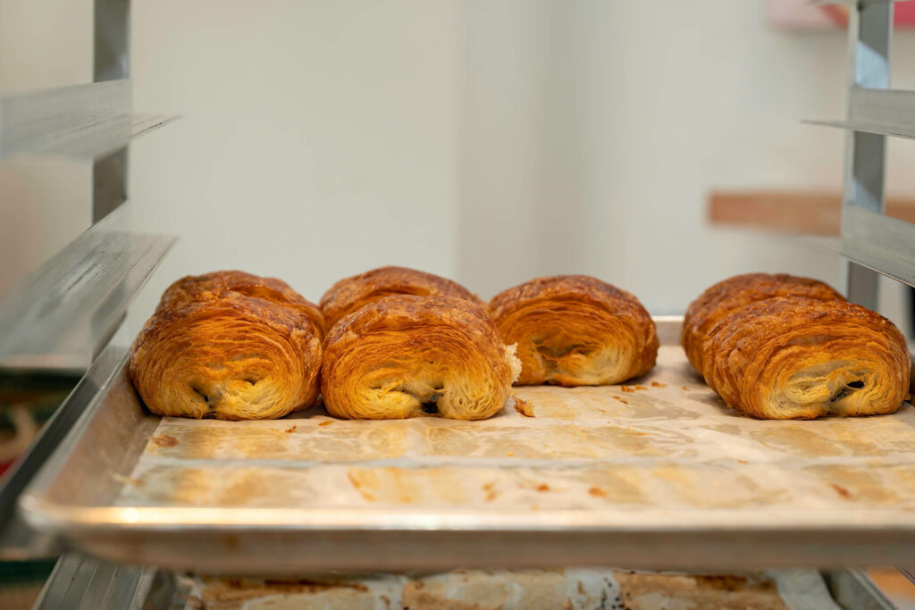 Row of pain au chocolat on a parchment-lined sheet tray at Butternut Bakehouse.
