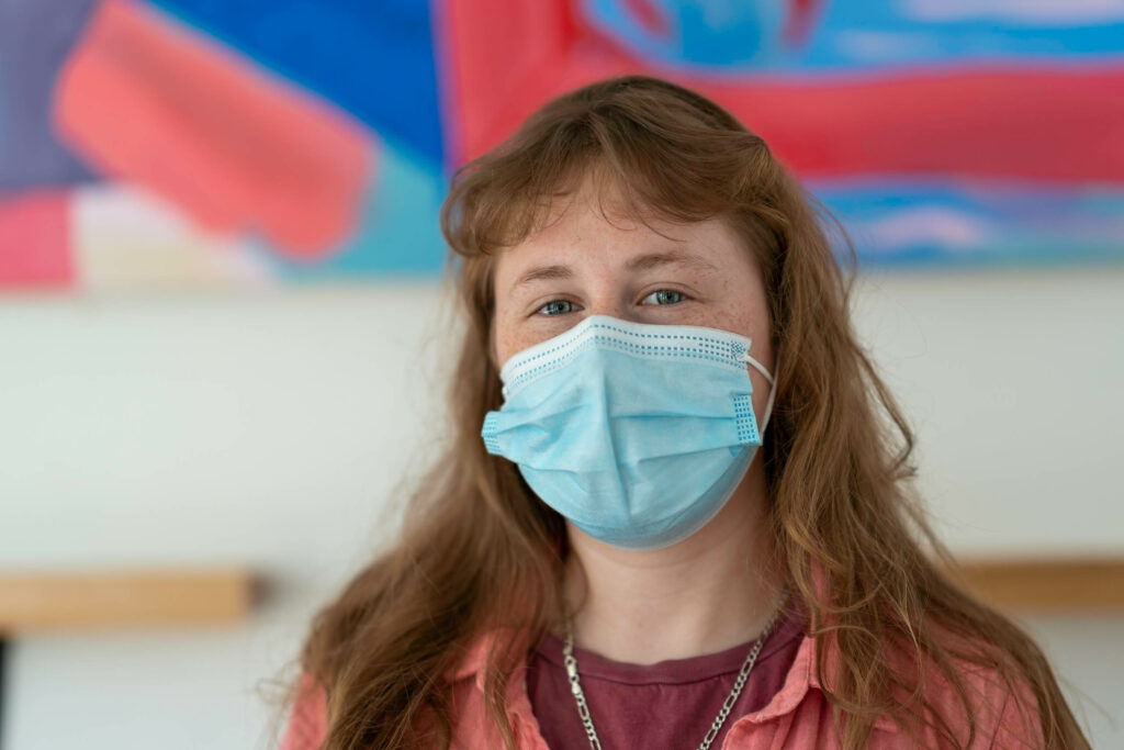 Butternut Bakehouse team member with long hair in a blue mask in front of a colorful abstract painting.