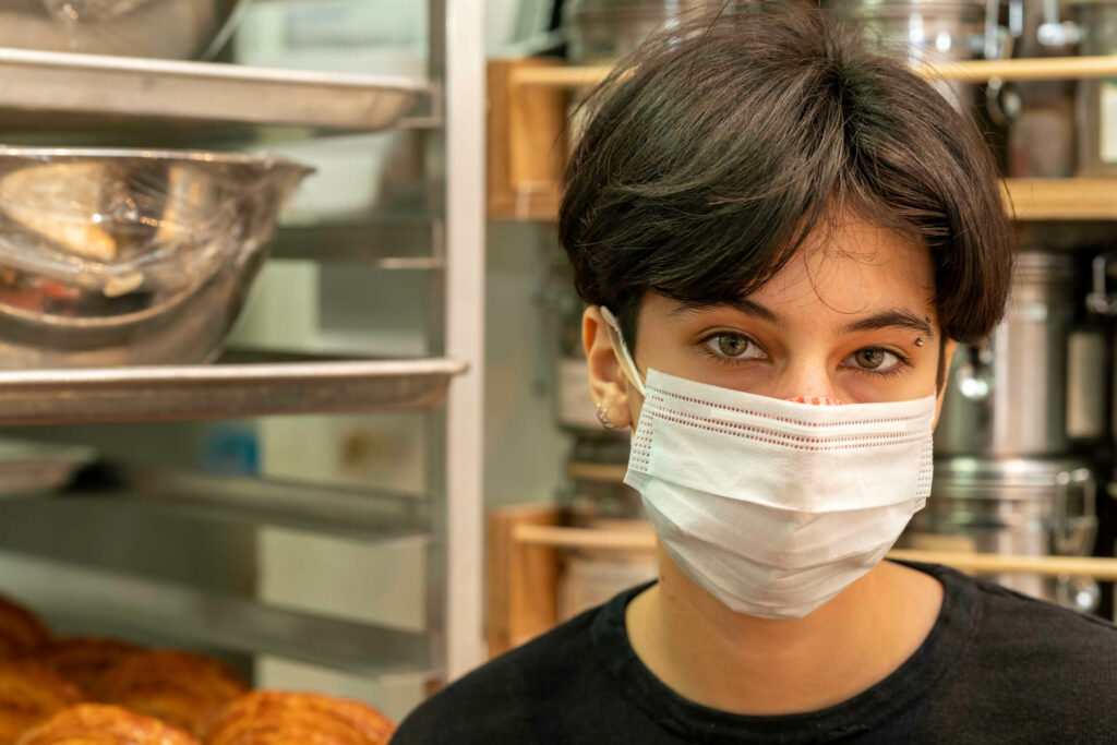 Butternut Bakehouse team member in a white mask in front of the kitchen rack.