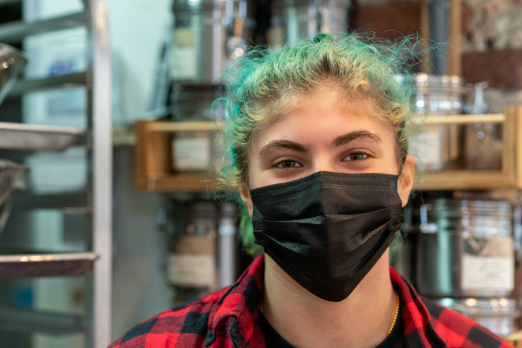 Butternut Bakehouse team member with green hair in a black mask and red plaid shirt.