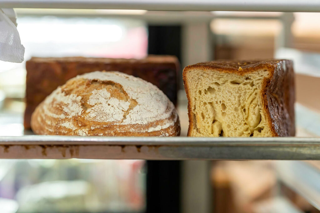 A sourdough boule beside a sliced brioche loaf on a bakery shelf at Butternut Bakehouse.