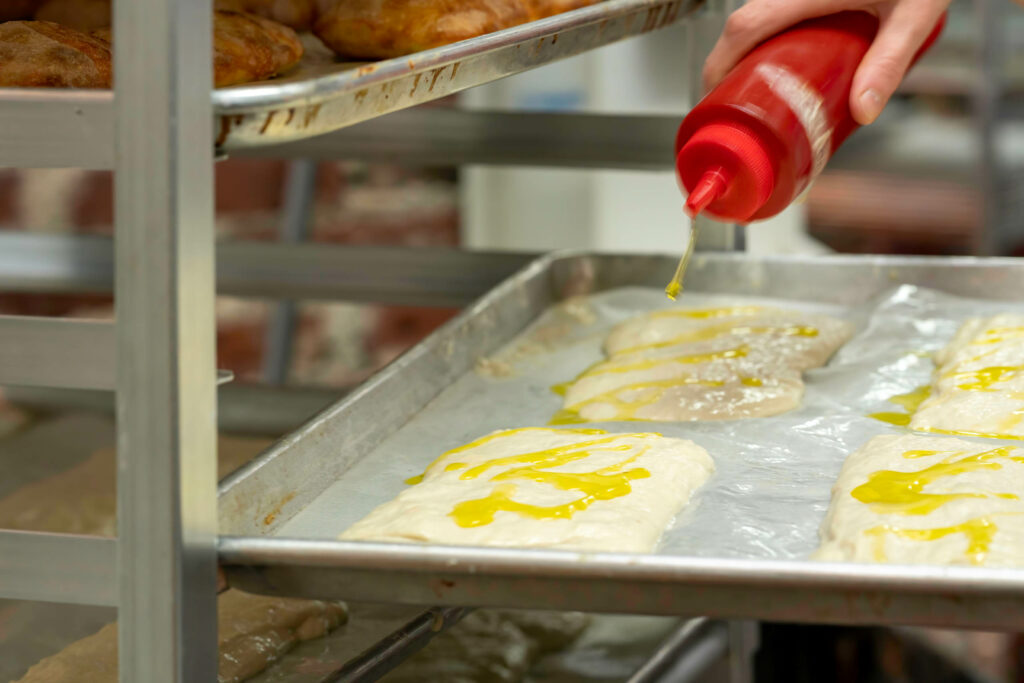 Olive oil being squeezed over trays of focaccia dough at Butternut Bakehouse.