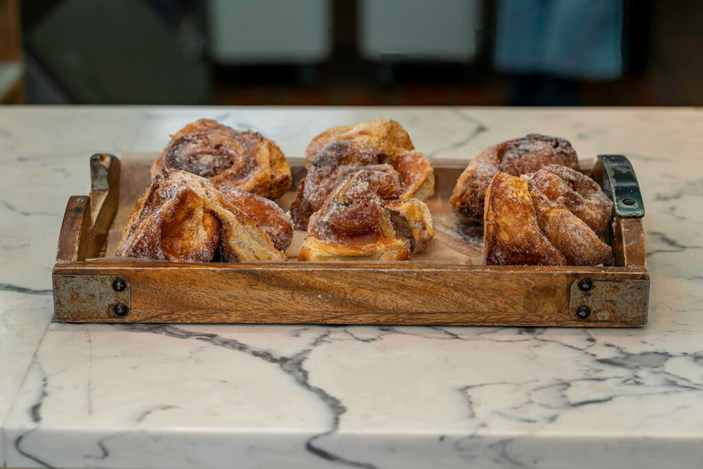 Tray of sugar-dusted morning buns on a wooden board on a marble counter at Butternut Bakehouse.