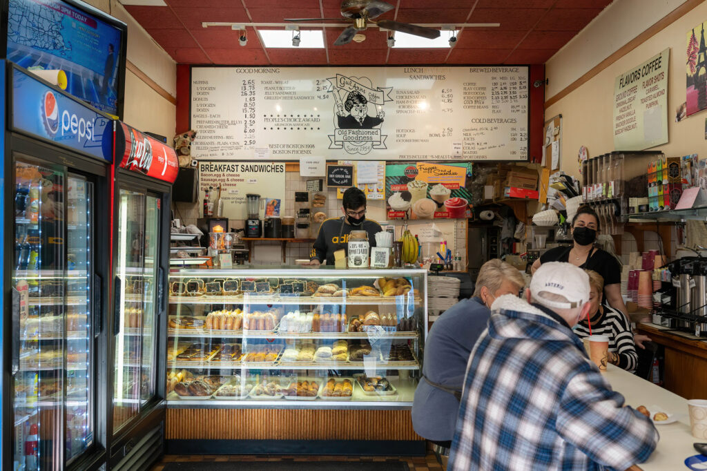 Inside Gail Ann Coffee Shop, customers at the counter with donut cases and the menu board above.