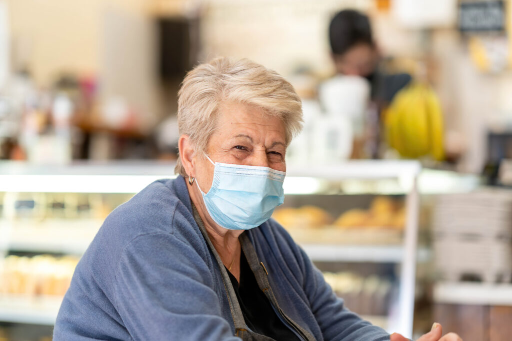 Owner of Gail Ann Coffee Shop smiling behind the counter in a blue mask.