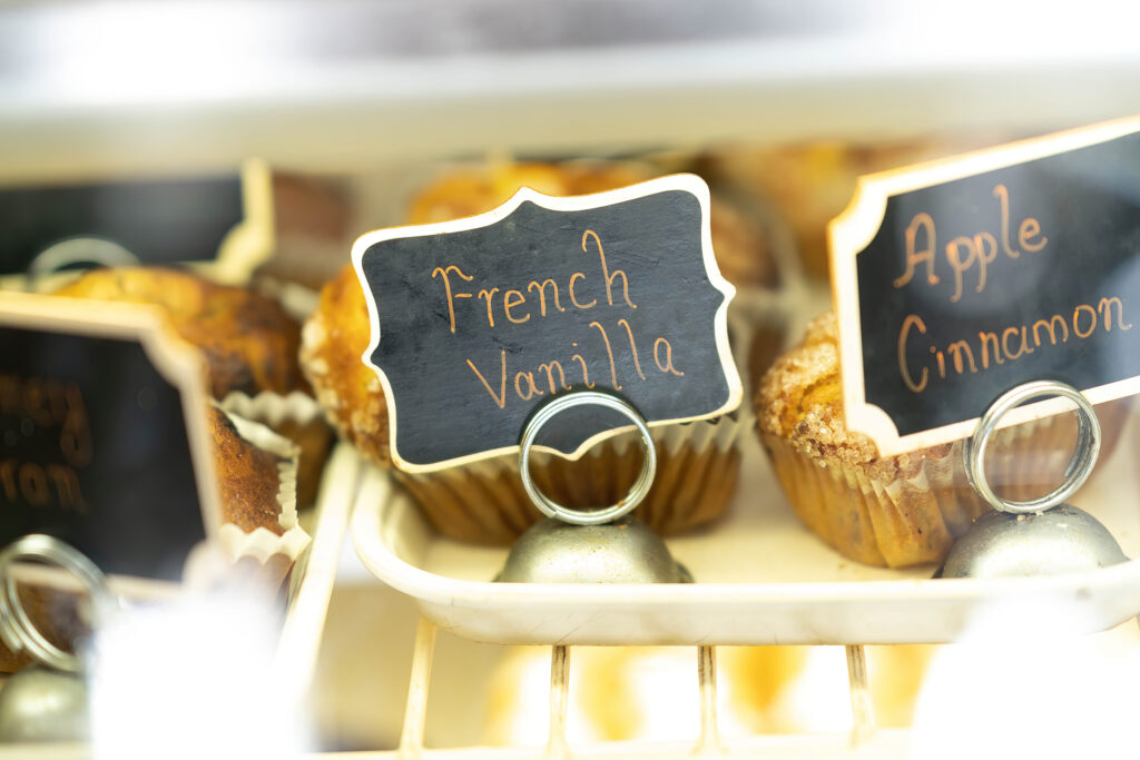 French Vanilla and Apple Cinnamon muffins with chalkboard labels in the Gail Ann Coffee Shop case.