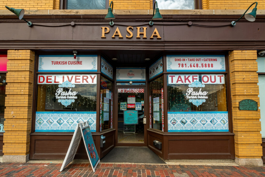 Pasha Turkish restaurant storefront with Delivery and Take Out window signs, Arlington MA.