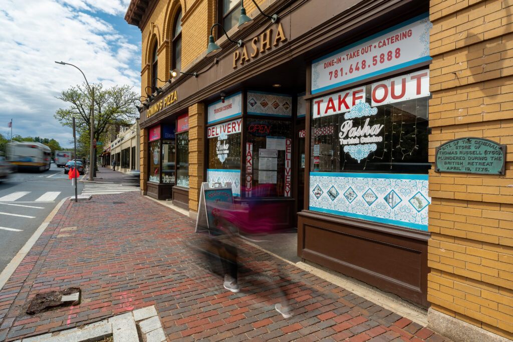 Pasha restaurant exterior on Massachusetts Avenue with a passing pedestrian blurred by motion.