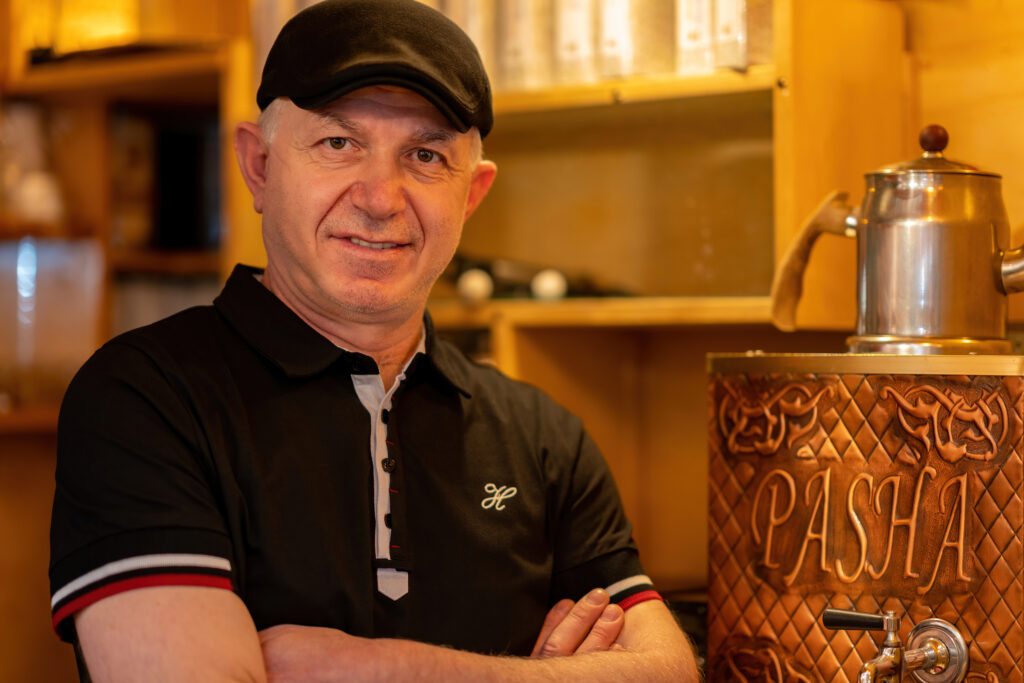 Halit Candemir with arms crossed beside the copper Pasha tea samovar.