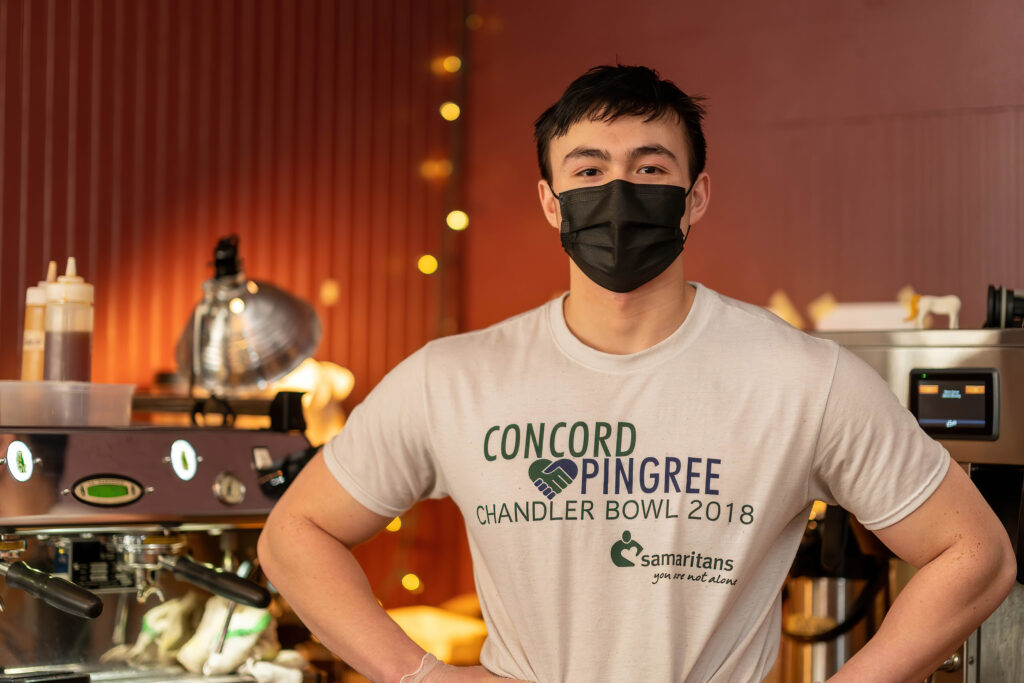 Barista in a black mask and Concord Pingree t-shirt at the espresso machine, The Roasted Granola.
