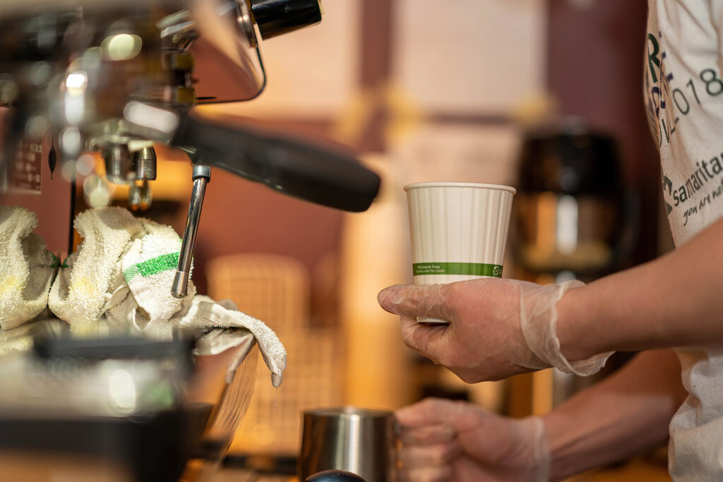 Barista holding a paper cup beside the steam wand at The Roasted Granola espresso bar.