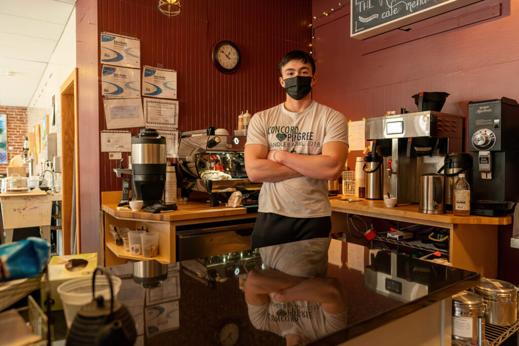 Barista in a mask standing arms crossed behind the coffee counter at The Roasted Granola.