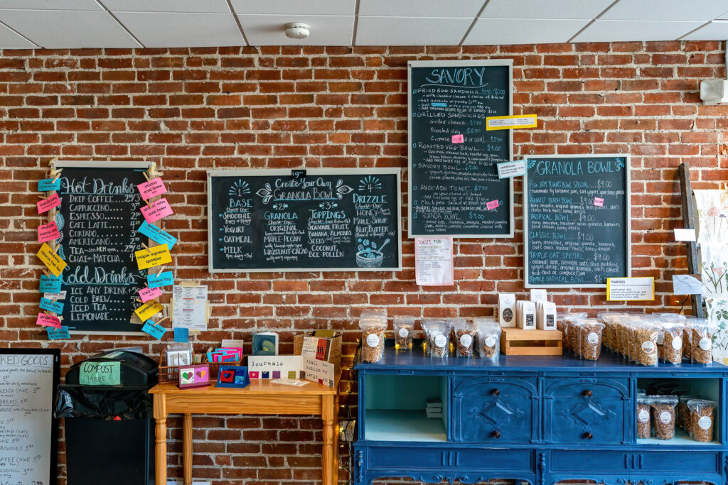 Brick wall of chalkboard menus and sticky notes above the retail shelf at The Roasted Granola.